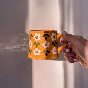 A unique handmade orange mug with floral decorations, perfect for gifting.